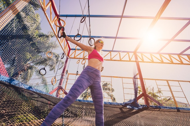 トレーニングキャンプで体操リングを使って運動する運動的な若い女性