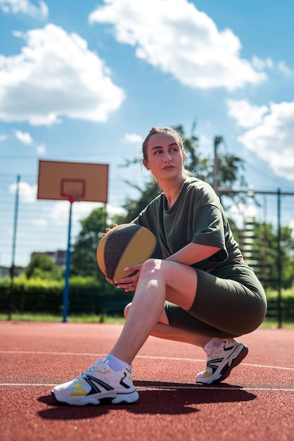 Photo athletic young woman posing with a ball on the court