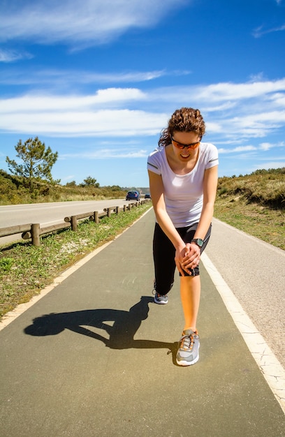 Athletic young woman in sportswear touching her knee by painful injury during a training outdoors. Sport injuries concept.