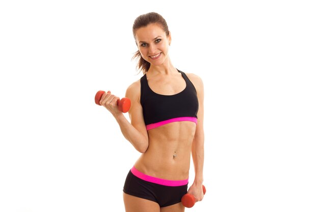 Athletic young woman at the top holding a dumbbell and smiling isolated on white wall