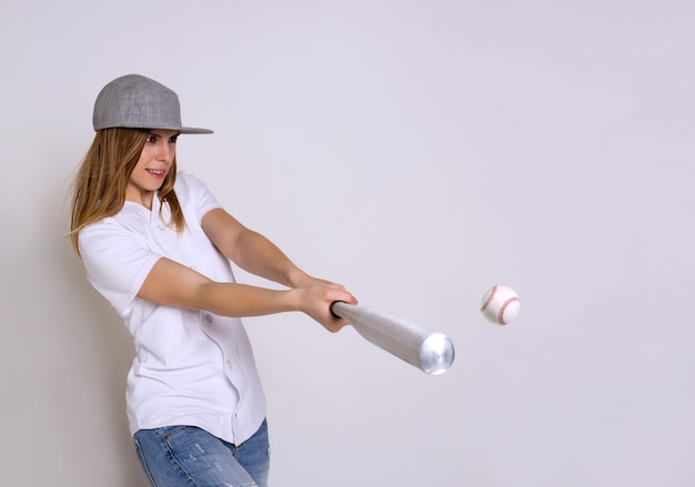 Athletic young woman with a baseball bat hits the ball