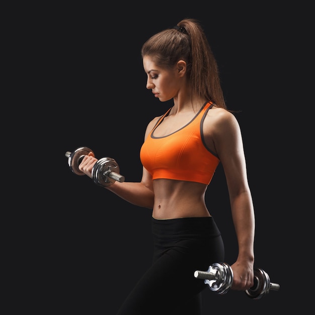 Athletic young woman with dumbbells on a black background. Studio shot, low key. Bodybuilding concept, copy space