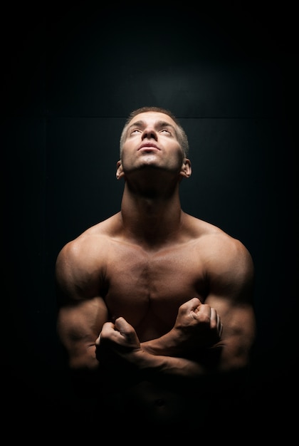 Athletically built young man looks up on a dark background