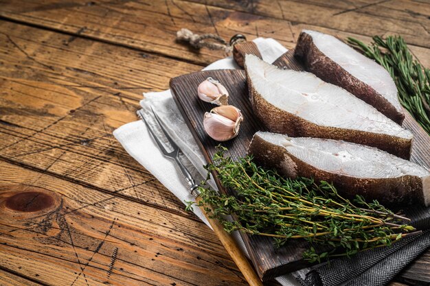 Atlantic halibut fish raw steaks on wooden board with herbs Wooden background Top view Copy space