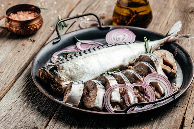 Atlantic mackerel fish or herring fish with salt, onion and spices on a metal tray. Food recipe background. Close up.