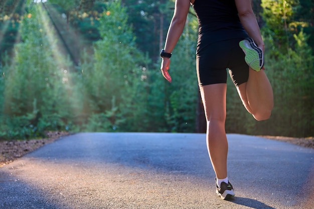 Atleet die haar benen en voeten strekt en zich voorbereidt om op een asfaltweg in het bos te rennen Actieve hardlooptraining in de zonnestralen en het concept van een gezonde levensstijl in de sport