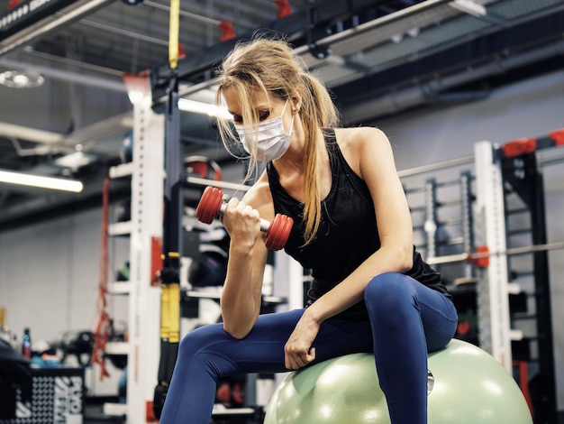 Atleet die tijdens een pandemie in de sportschool traint en een beschermend gezichtsmasker draagt