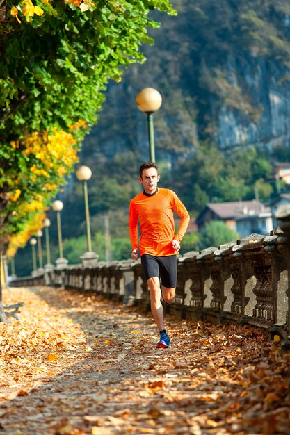 Atleet man loopt in de herfst tussen de bladeren