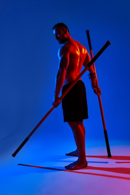 Atleet mannen silhouet met stick opleiding karate met behulp van sport tool in studio op kleurrijke lichten achtergrond