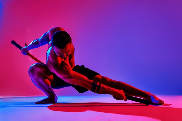 Atleet mannen silhouet met stick opleiding karate met behulp van sport tool in studio op kleurrijke lichten achtergrond