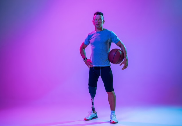 Atleet met een handicap of geamputeerde op de achtergrond van de gradiëntstudio in neon. Basketballer