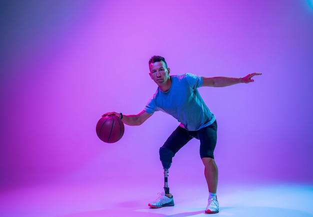 Atleet met een handicap of geamputeerde op de achtergrond van de gradiëntstudio in neon. Basketballer