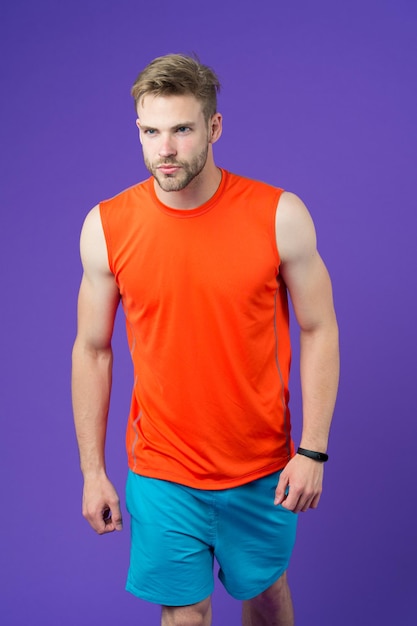 Atleet met sexy gespierd lichaam runner training voor marathon sport en fitness concept man met getrimde baard dragen sportieve oranje vest en blauwe korte broek sportman geïsoleerd op paarse achtergrond