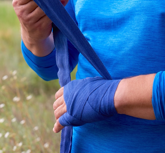 Atleet staan en wikkel zijn handen in blauw textiel elastisch verband voor de training