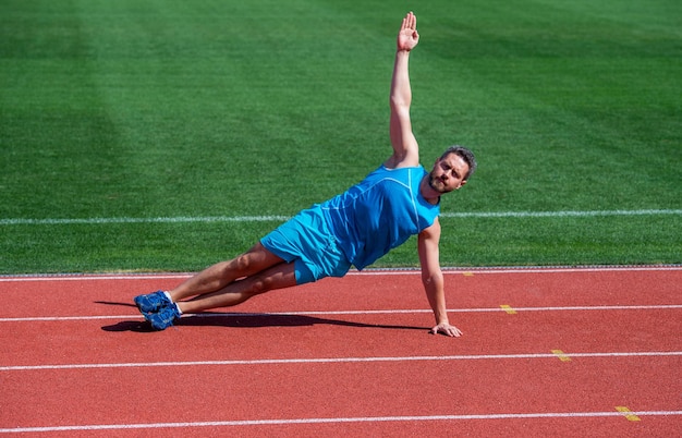 Atleet traint zijn kernspieren man doet rekoefeningen op stadion fitness gym buiten Vol energie atletische man opleiding sport mannelijke kracht en macht sportman in zijplank