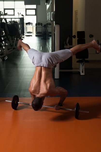 Atleet uitoefening handstand push-ups op barbell in sportschool