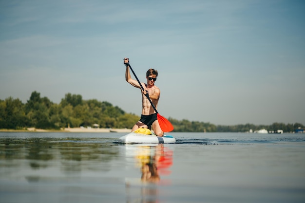 Foto atleet zwemt de rivier af op een sup board en peddelt actief met een geconcentreerd gezicht