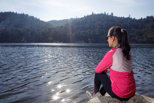 Atleta descansando a la orilla de un lago sentada sobre una piedra despus de correr en el bosque