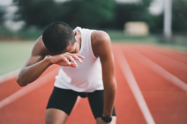 Atleten sport man loper dragen witte sportkleding moe zweet afvegen en rusten na het oefenen op een atletiekbaan in een stadion runner sport concept