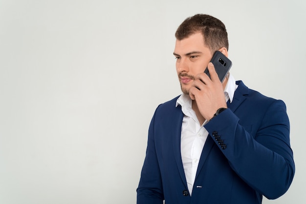 Atletisch gebouwde jonge zaken man in een pak en zwart shirt praten over een mobiele telefoon op een witte achtergrond geïsoleerd