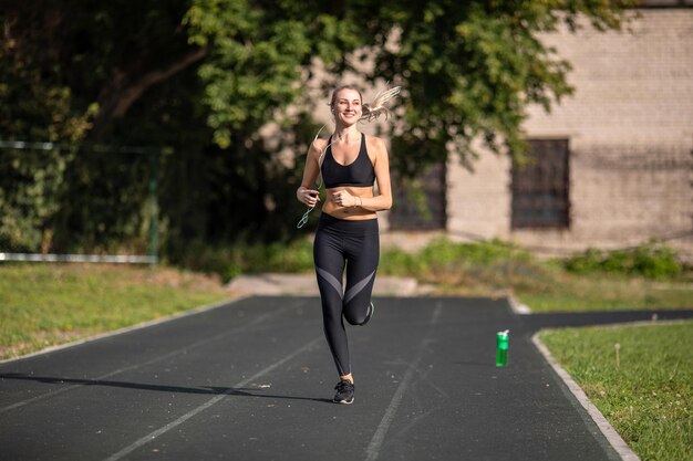 Atletisch meisje met blije gezichtsuitdrukking in rug-t-shirt en legging in het stadion met een fles water