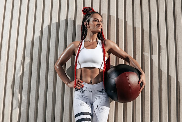 Atletisch vrouwenportret met med bal Kracht en motivatie Foto van sportieve vrouw in modieuze sportkleding