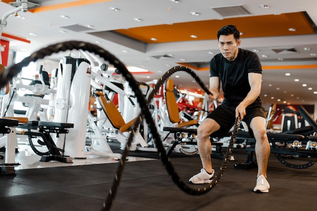 Atletische Aziatische jongeman doet wat fitnessoefeningen met slagtouw bij fitness gym Gespierde krachtige agressieve training Concept voor het uitoefenen van fitness en een gezonde levensstijl