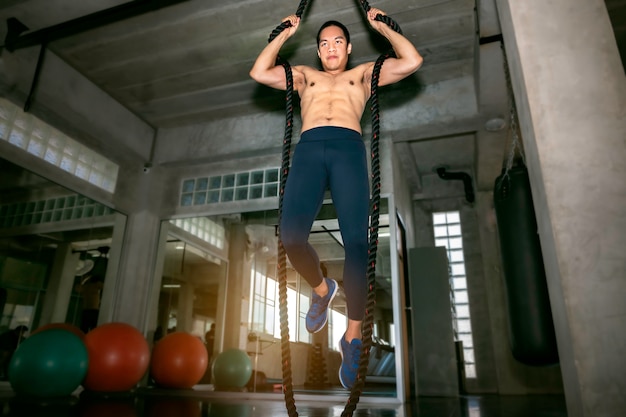 Atletische aziatische man training touw klimmen oefening op sportschool.