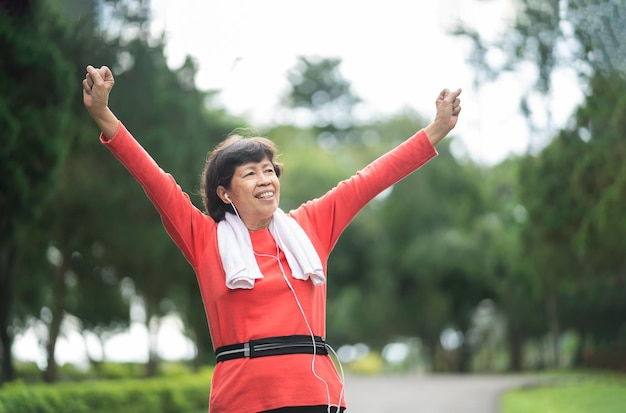 Atletische aziatische senior vrouw 60s lachende handen omhoog en blij vrolijk met succes en joggen