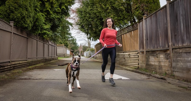 Atletische blanke volwassen vrouw die buiten rent met een bokserhond