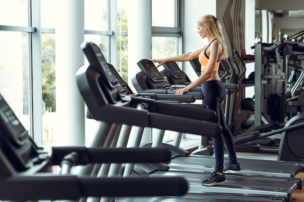 Atletische blonde vrouw draait op loopband op sportschool.