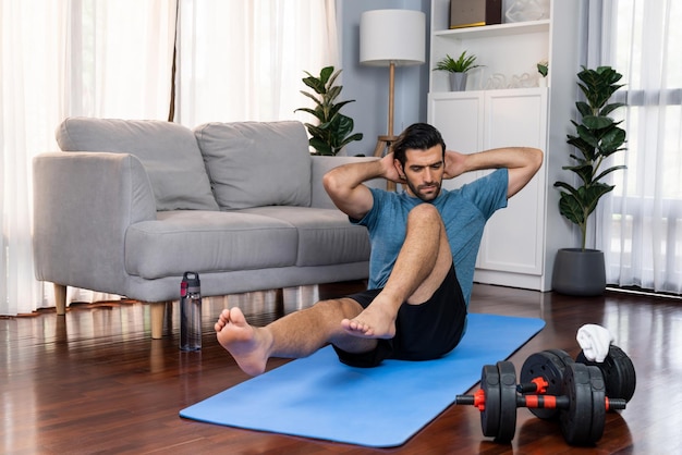 Atletische en sportieve man doet crunch op fitnessmat bij vrolijkheid thuis