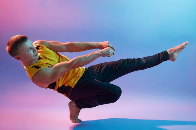 Atletische gespierde jonge man beoefenen van yoga tegen neon muur, gele t-shirt en zwarte broek dragen