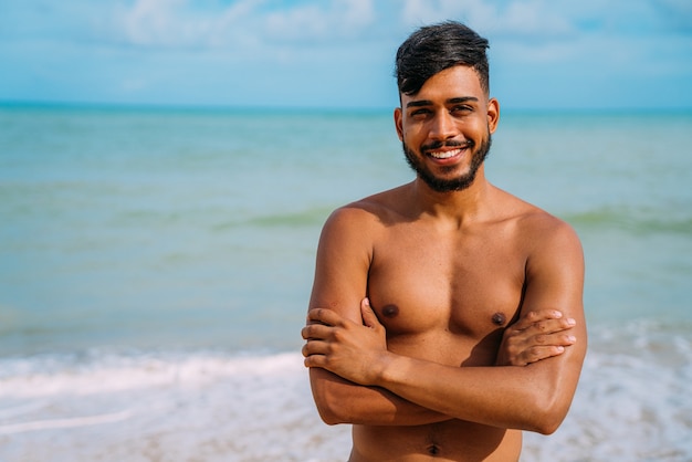 Atletische jonge Latijns-Amerikaanse man op het strand met gekruiste armen