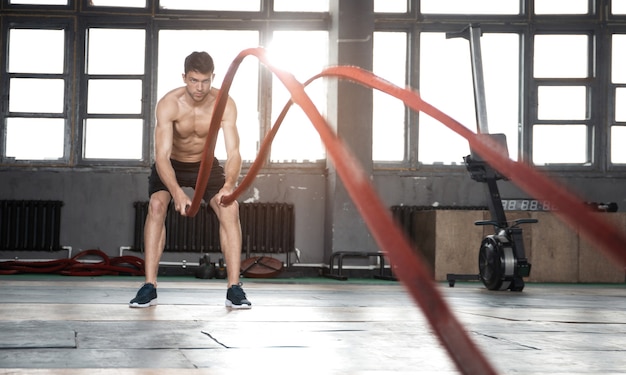 Atletische jonge man met slag touw doen oefening in functionele training fitness gym.