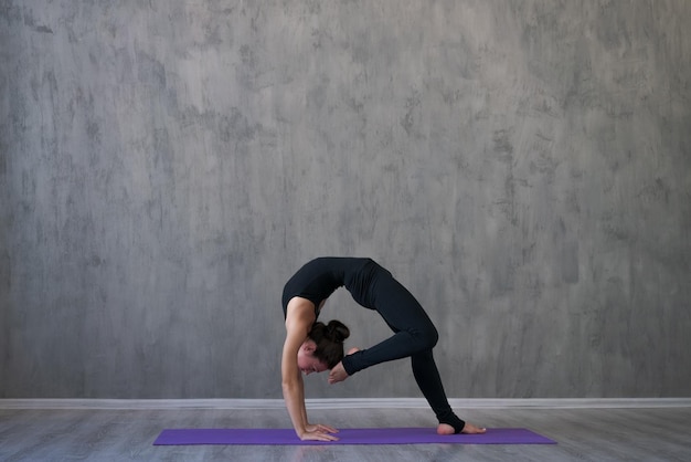 Atletische jonge vrouw beoefent yoga met het gezicht naar beneden geïsoleerd op een grijze muur