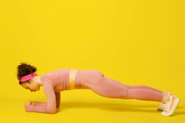 Atletische jonge vrouw die oefeningen doet over gele studioachtergrond