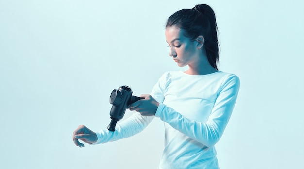 Atletische jonge vrouwelijke hand masseren met handmassage pistool in neonlicht, herstel na de training