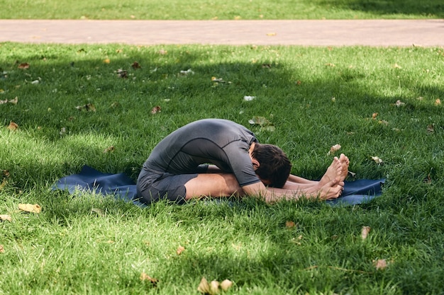 Foto atletische jongeman in sportkleding doet yoga in het park