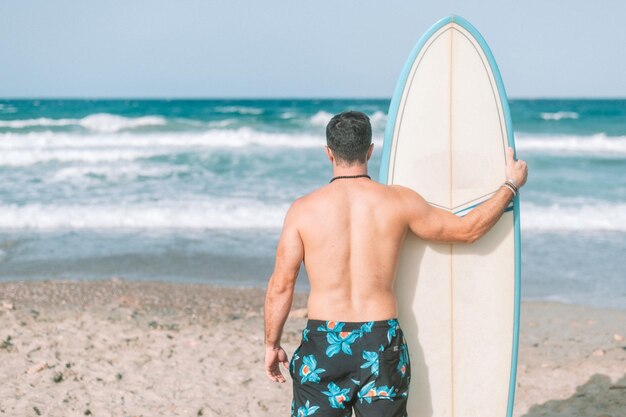 Foto atletische jongeman surfen op het strand