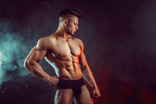 Atletische man buigen spieren met rook. Sterke bodybuilder met perfecte buikspieren.