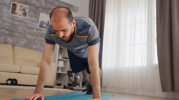 Atletische man die bergbeklimmers doet die thuis op yogamat trainen en sportkleding dragen.