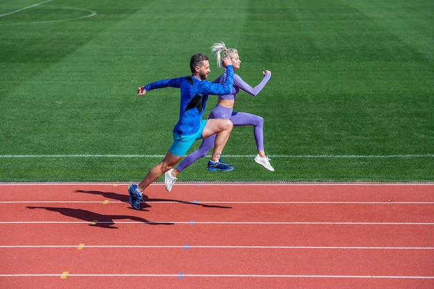 Atletische man en sexy vrouw concurreren in sprint. mannelijke en vrouwelijke coach op de atletiekbaan van het stadion. gezonde levensstijl. marathon snelheid. sportpaar loopt snel om te winnen. succesvolle fitnesssprinters.