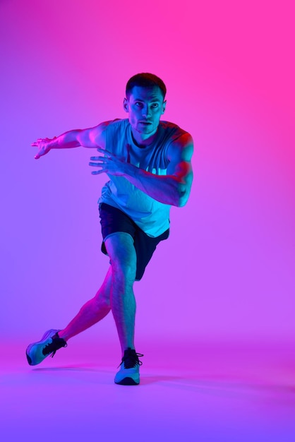 Atletische man in comfortabele sportkleding met gespierde lichaamstraining tegen een gradiënt roze achtergrond