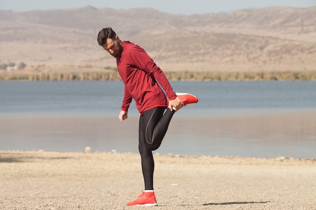 Atletische man in sportkleding die zich uitstrekt in de natuur