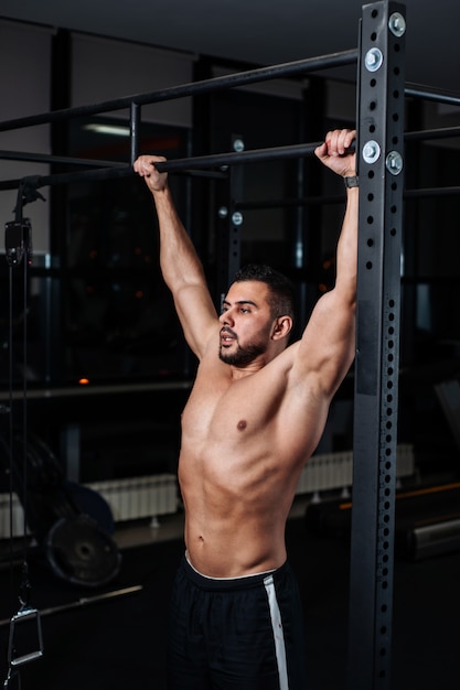 Atletische man maken pull-up oefeningen op een lat in de sportschool