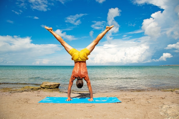 Atletische man op strand doen fitness yoga oefening.