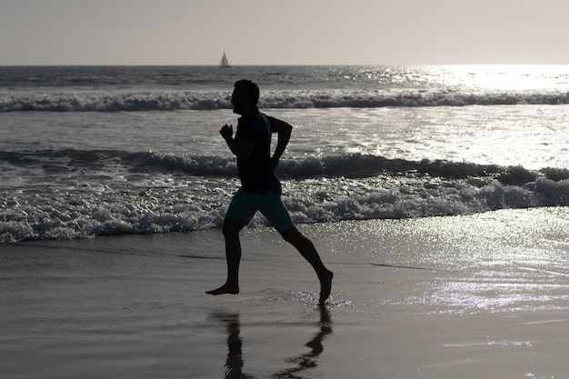 Atletische man runner silhouet lopen op zomer strand met zeewater en zon, motivatie.