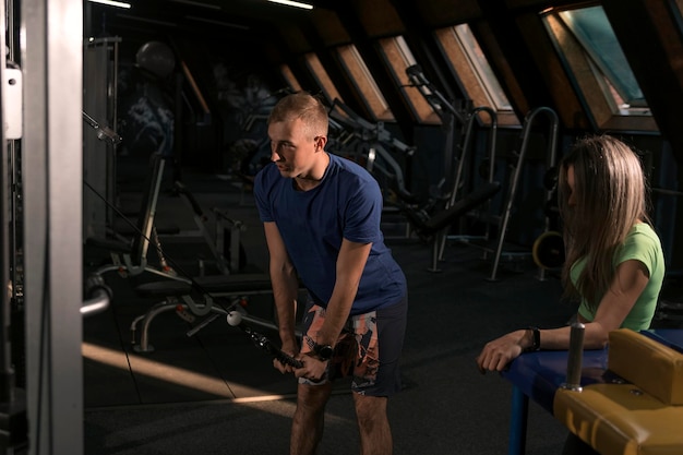 Atletische man toont oefening voor triceps op simulator Fitnesstrainer voert persoonlijke training uit in de sportschool