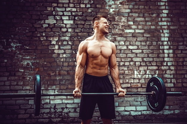 Atletische man uit te werken met een barbell. Kracht en motivatie. Biceps oefenen.